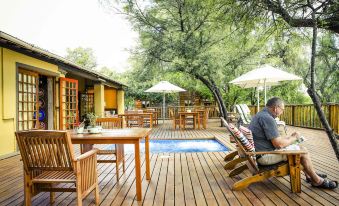 a man is sitting in a chair on a wooden deck near a pool and surrounded by lounge chairs at Riverside Guest Lodge