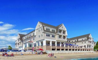 a large building on the beach , with people relaxing in the sand and umbrellas set up at Beauport Hotel Gloucester