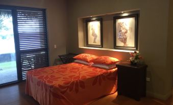 a well - lit bedroom with a bed , two nightstands , and a window , decorated with a red comforter and pillows at Mangaia Villas
