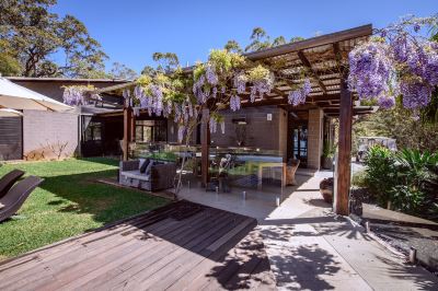a wooden house with a patio , dining table , and fireplace , surrounded by greenery and flowers at Spicers Sangoma Retreat