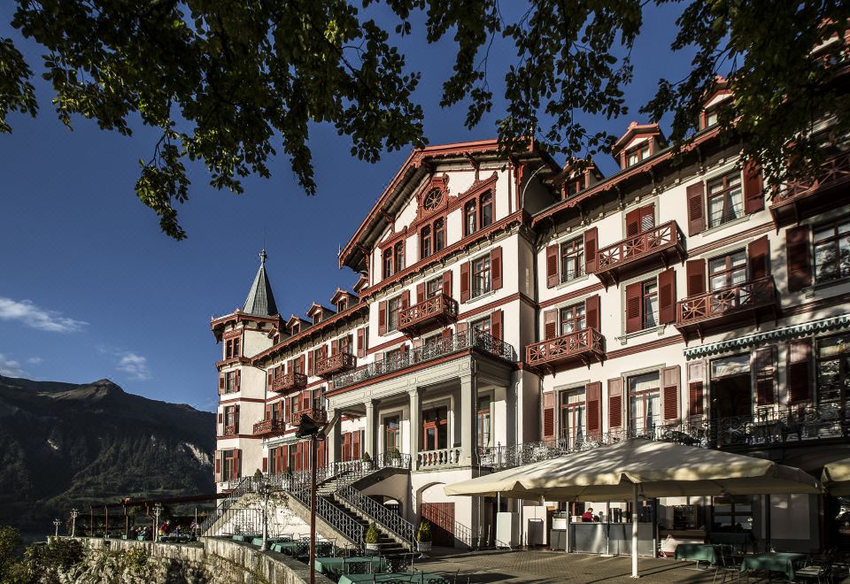 a large red and white building with multiple balconies , situated on a hillside overlooking a body of water at Grandhotel Giessbach