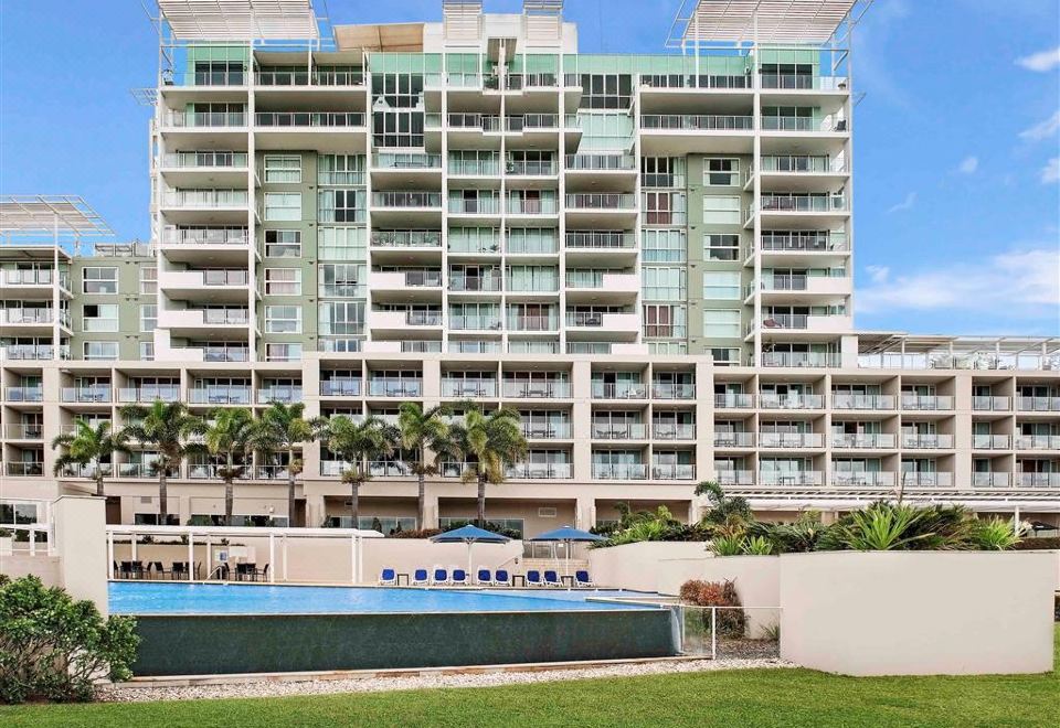 a modern apartment building with a swimming pool and lush green grass , under a clear blue sky at Pelican Waters Resort