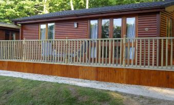 a wooden house with a deck and railing is surrounded by trees in the daytime at Watermouth Lodges