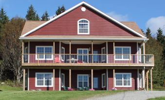a two - story red wooden building with a balcony , surrounded by trees and grass , under a clear blue sky at The Fiddle and the Sea Bed and Breakfast