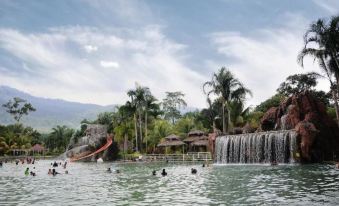 a group of people are enjoying a water park with a waterfall and pool , surrounded by lush greenery at Felda Residence Hot Springs