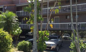 a parking lot with several cars parked in front of a multi - story building , surrounded by trees at Holland Park Motel