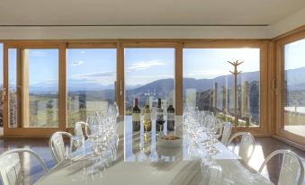 a dining room with a large dining table surrounded by chairs , all facing a panoramic view of the mountains at Trossos del Priorat