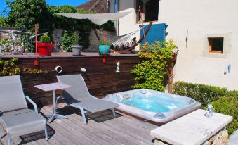 a backyard with a hot tub , lounge chairs , and a wooden deck , surrounded by lush greenery at Le Manoir