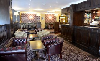 a cozy bar with leather couches , chairs , and a bar area , decorated with floral wallpaper and a clock on the wall at Buckatree Hall Hotel