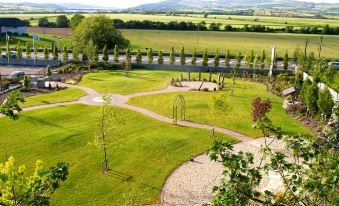 a lush green lawn surrounded by trees and benches , with a view of the countryside in the background at An Grianan Hotel