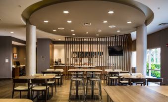 a modern restaurant with wooden tables and chairs , a large screen on the wall , and a bar area at SpringHill Suites Vero Beach
