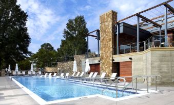 a large outdoor pool surrounded by lounge chairs and umbrellas , with a stone building in the background at Raleigh Marriott Crabtree Valley