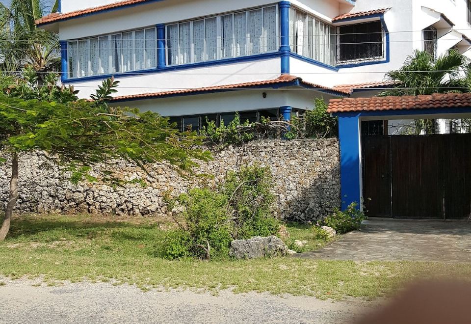 a large white house with blue trim , situated on a dirt road surrounded by trees and bushes at Blue Rooms