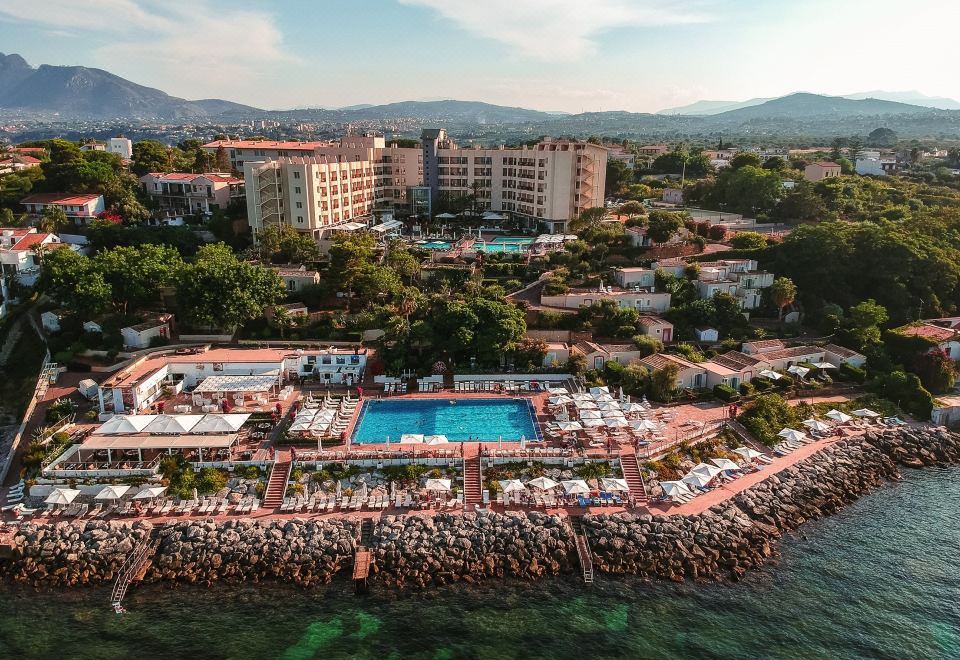 aerial view of a resort with a large pool surrounded by lounge chairs and umbrellas , situated on a beach near a body of water at Domina Zagarella Sicily