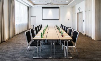 a conference room with a long table surrounded by chairs and a projector screen on the wall at Park Inn by Radisson Krakow
