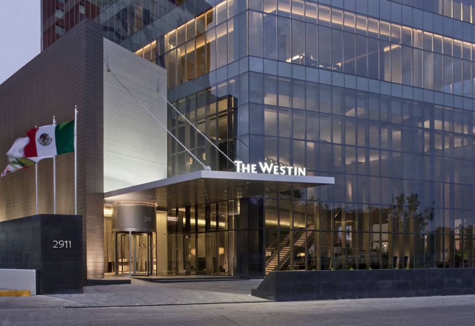 a modern hotel building with a large sign above the entrance , illuminating the surrounding area at The Westin Guadalajara