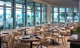 a modern restaurant with large windows offering a view of the ocean , and several dining tables set up for guests at Treasure Island Beach Resort