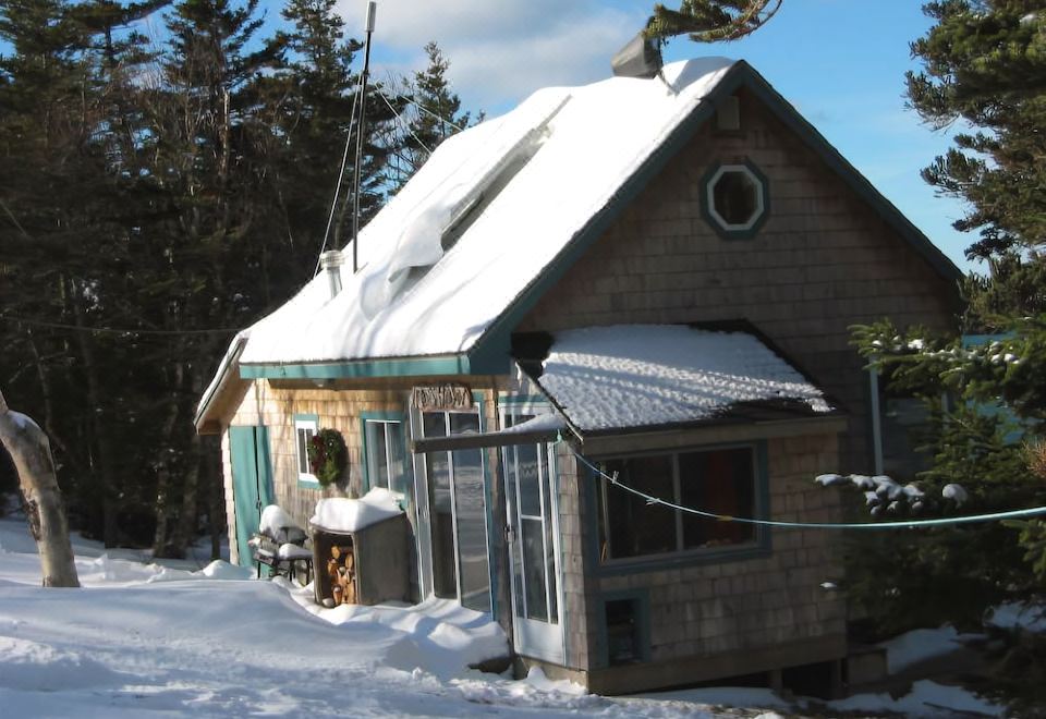 a small wooden house surrounded by snow , with a blue sky in the background and trees in the foreground at Adventure High