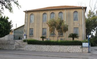 a large building with arched windows and a red tile roof is shown in front of a stone wall at Like Home Gedera