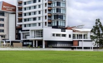 a large white building with a green lawn in front of it , surrounded by trees at Mercure Sydney Liverpool