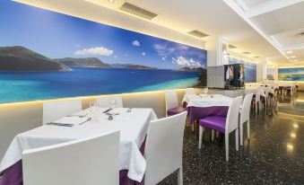 a dining room with white tables and chairs , purple tablecloths , and a large mural of the ocean at Globales Palmanova