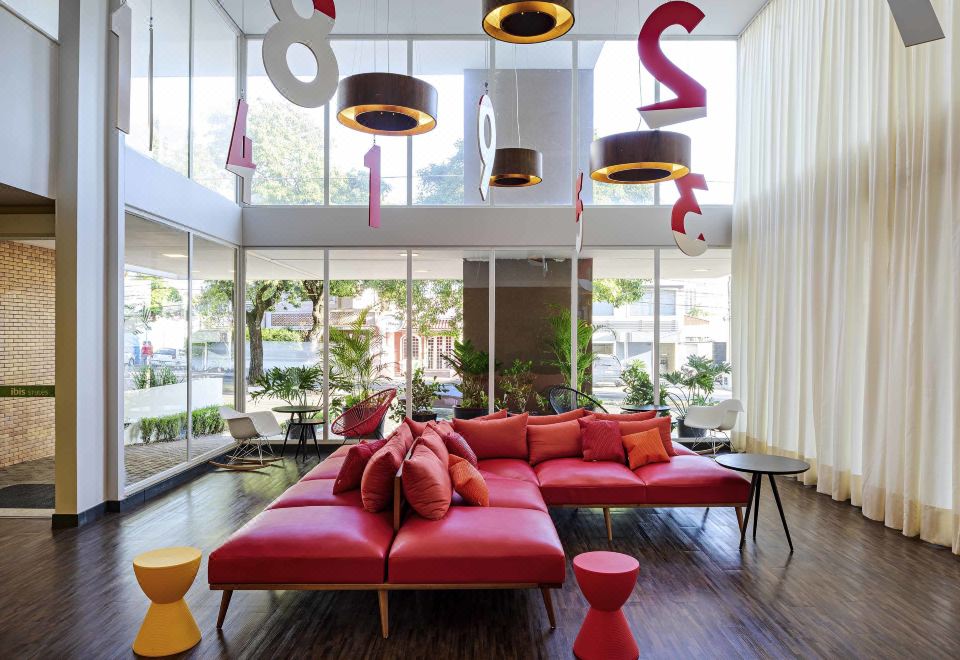 a modern living room with a large red couch , multiple chairs , and a dining table at Ibis Styles Piracicaba