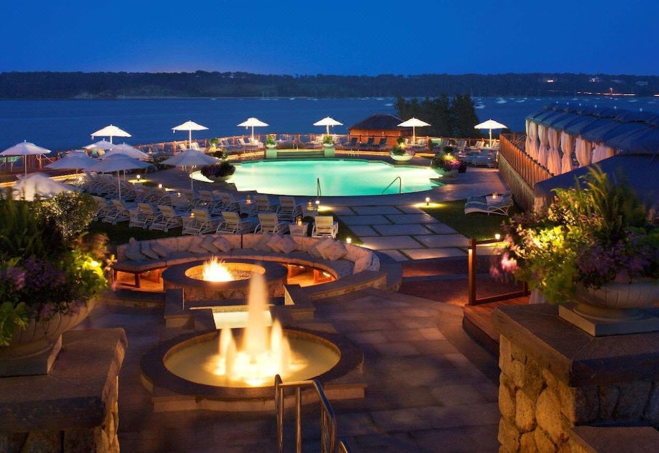 an outdoor pool area with a fire pit and umbrellas , surrounded by chairs and lounge chairs at Wequassett Resort and Golf Club