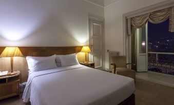 a neatly made bed with white sheets and pillows , situated in a room with a chair , lamp , and door at Hotel Astoria