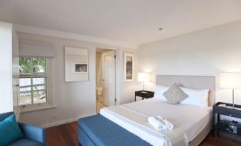 a large bed with white linens and a blue ottoman in a hotel room with wooden floors at Cockatoo Island Accommodation