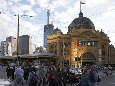 a bustling city scene with a large crowd of people walking around a building , some carrying umbrellas and others waiting to board at Ibis Melbourne Hotel and Apartments