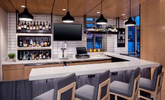 a modern bar with a curved counter , white tile backsplash , and black pendant lights above it at Hyatt House Charleston/Mount Pleasant
