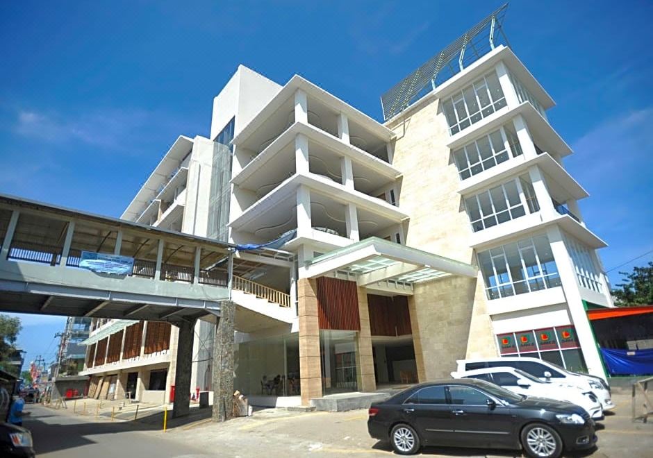 a modern building with multiple floors , cars parked in front , and cars going through a covered entrance at Laut Biru Resort Hotel