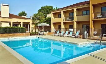 a swimming pool surrounded by multiple buildings , with lounge chairs and umbrellas placed around the pool area at Courtyard Richmond West