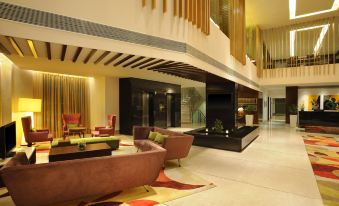 a modern hotel lobby with a curved couch , multiple seating areas , and a glass elevator at Four Points by Sheraton Ahmedabad