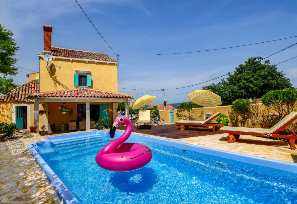 a swimming pool with a pink flamingo float in the water , surrounded by a yellow house and a clear blue sky at Villa Mare