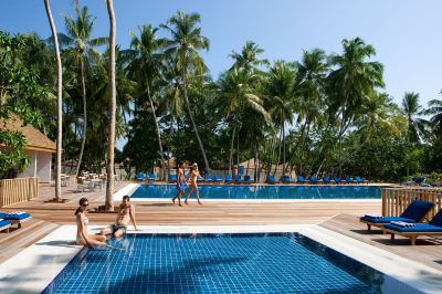 a tropical resort with a large swimming pool , umbrellas , and people relaxing on the deck , under a clear blue sky at Vilamendhoo Island Resort & Spa