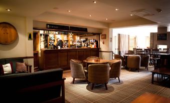 a cozy bar with a wooden counter , several chairs , and a person behind the counter at Lancaster House Hotel