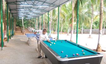 a man is playing a game of pool on a green table under a covered area at Bluebay Beach Resort