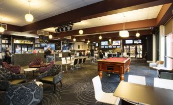 a bar with various chairs , tables , and couches , as well as a pool table in the background at Nightcap at Skyways Hotel