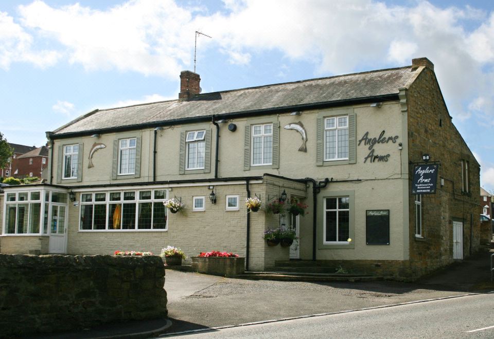 "the acers arms pub , a white building with a sign that reads "" acers arms ,"" surrounded by potted plants and trees" at Anglers Arms