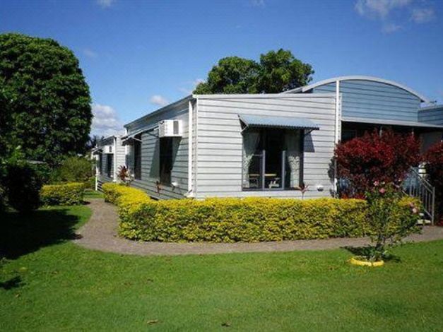 a small , modern house surrounded by green grass and trees , located in a residential area at Tin Can Bay's Sleepy Lagoon Motel