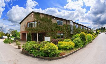 a large brick building with ivy growing on its side , surrounded by a lush garden at Best Western Plus Centurion Hotel