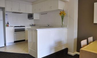 a modern kitchen with white cabinets and appliances , a black countertop , and a vase of flowers at Coogee Sands Hotel & Apartments