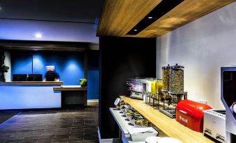 a modern hotel lobby with a dining area featuring a breakfast bar and a kitchenette at ibis budget Casula Liverpool