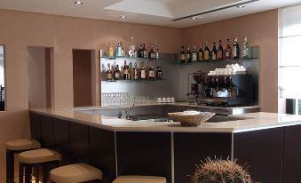 a bar with a variety of liquor bottles and cups on shelves , along with a counter and stools at Hotel Nord