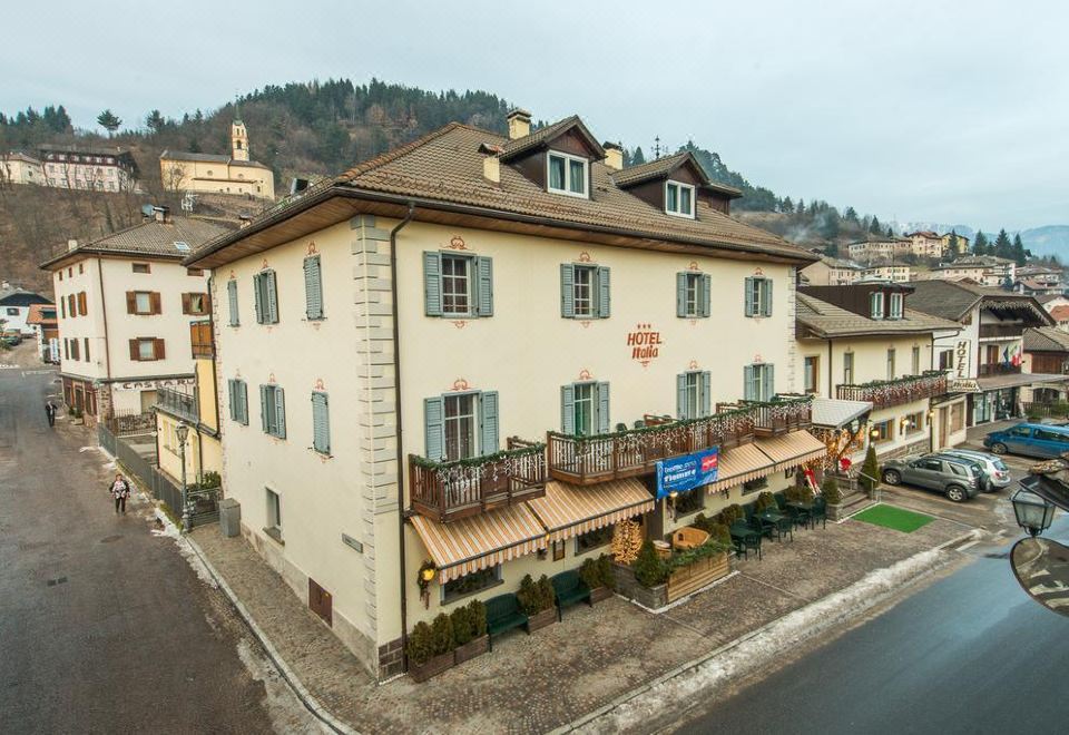 a large white building with multiple balconies and windows , located on a street with mountains in the background at Hotel Italia