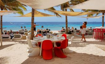 a restaurant with red chairs and white tables is set up on a sandy beach near palm trees at Papagayo Beach Resort