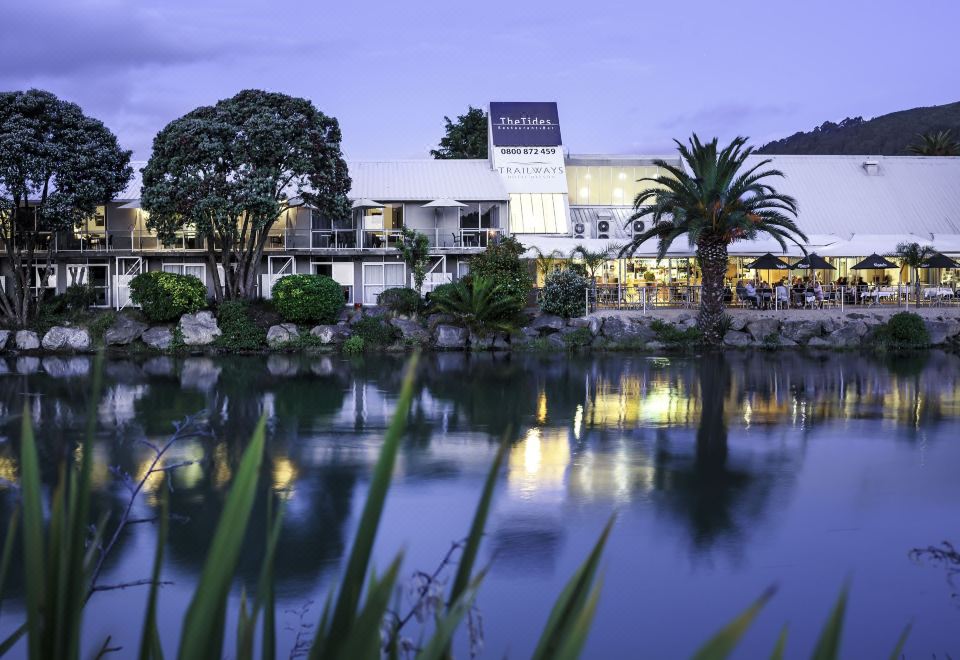 a large building with a blue sign is reflected in the water , surrounded by trees and palm trees at Tides Hotel