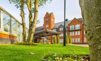 a large brick building with a clock tower , surrounded by a grassy area and trees at The Park Royal Hotel & Spa