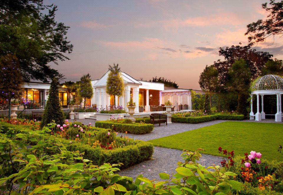 a beautiful white house surrounded by lush greenery , with a garden in front of it at The Keadeen Hotel